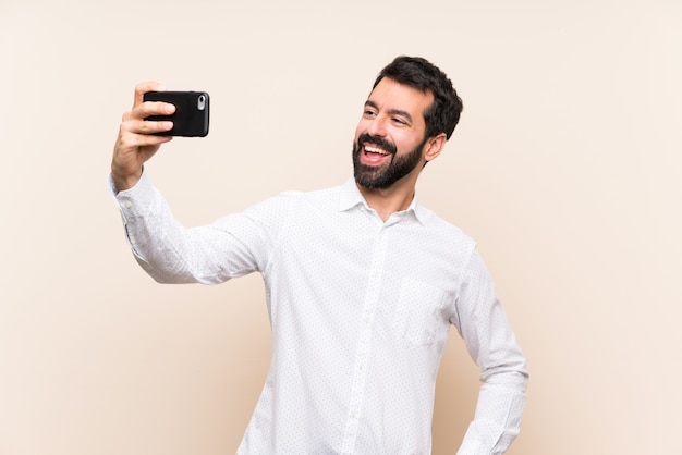 Giovane con la barba che tiene un cellulare che fa un selfie