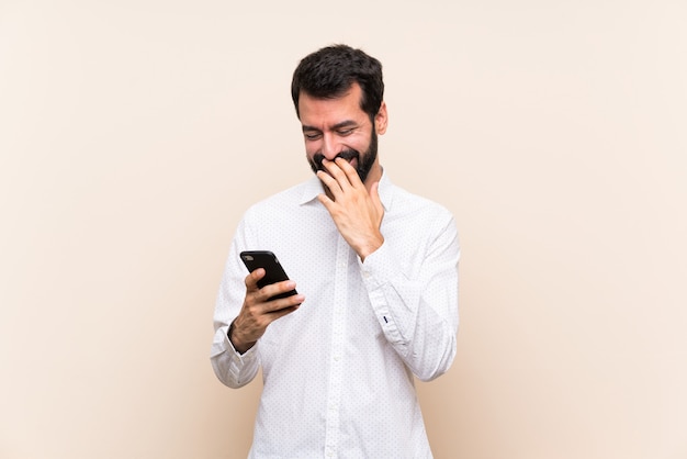 Giovane con la barba che tiene un cellulare che sorride molto