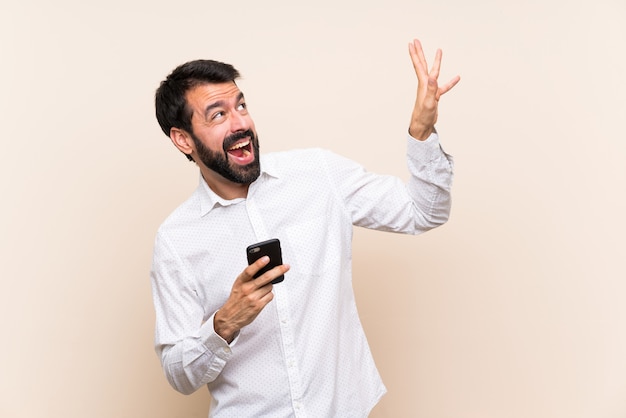 Giovane con la barba che tiene un cellulare nervoso e spaventato