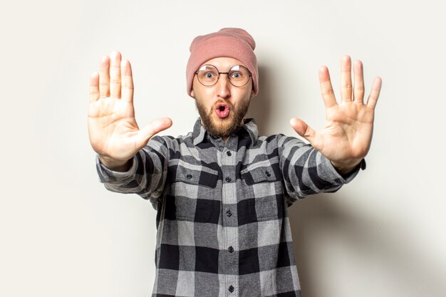 giovane con la barba in un cappello, una camicia a quadri stese le mani davanti a sé con i palmi delle mani verso lo spettatore su un bianco isolato. Basta gesto, basta