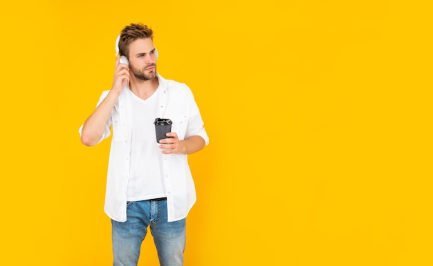 Giovane con la barba lunga in cuffie che beve caffè su sfondo giallo con stile di vita dello spazio della copia