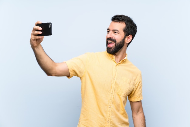 Giovane con la barba sopra il blu isolato che fa un selfie