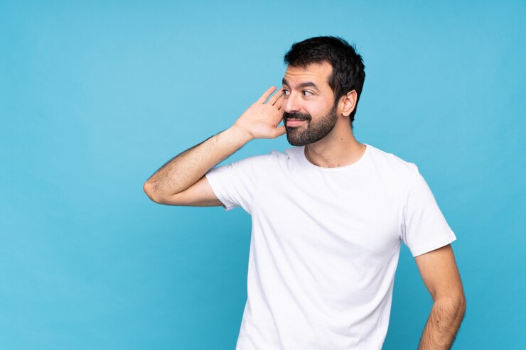 Foto giovane con la barba sopra l'isolato blu che ascolta qualcosa mettendo la mano sull'orecchio