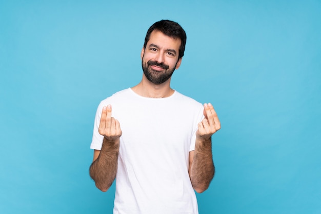 Giovane con la barba sopra la parete blu isolata che fa gesto dei soldi