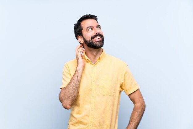 Giovane con la barba sopra la parete blu isolata che pensa un'idea