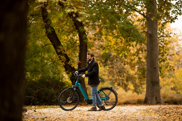 Giovane con la bicicletta elettrica nel parco autunnale di te