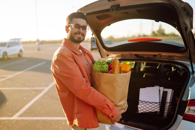 Giovane con la borsa della spesa piena di verdure vicino all'auto Bell'uomo dopo lo shopping