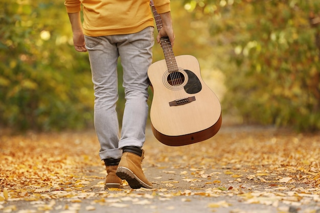 Giovane con la chitarra che cammina nel primo piano del parco di autunno