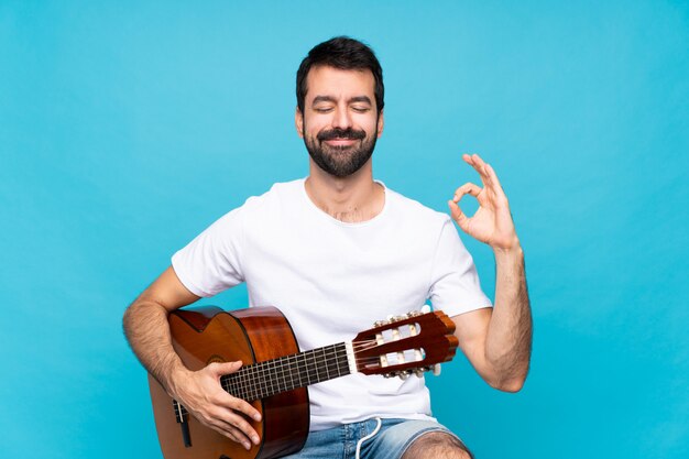 Giovane con la chitarra sopra l'azzurro nella posa di zen