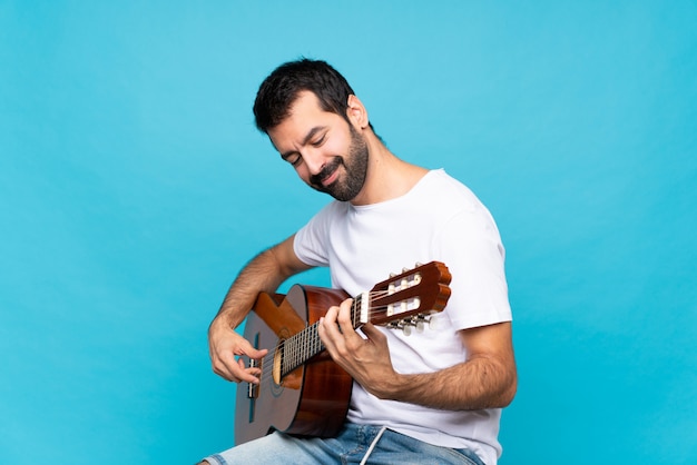 Giovane con la chitarra sopra la parete blu isolata