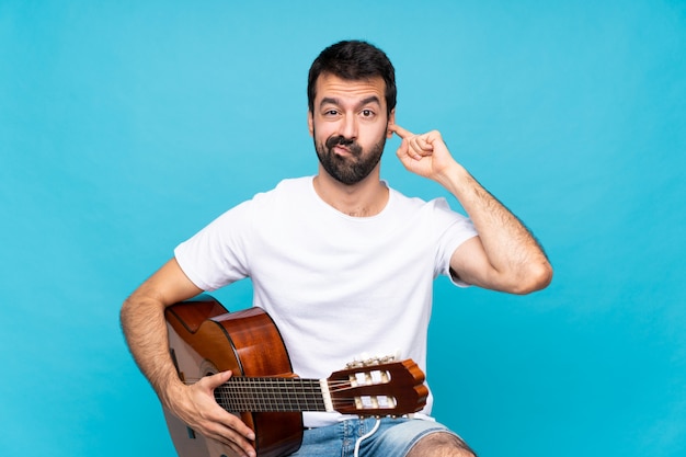 Giovane con la chitarra sopra le orecchie frustrate e di copertura blu