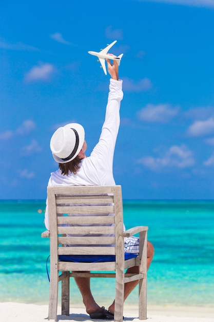 Giovane con la miniatura di un aeroplano in spiaggia tropicale