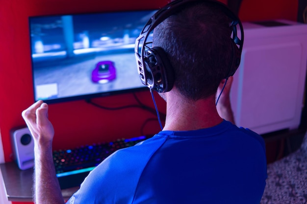 Giovane con le cuffie che gioca a videogiochi su un computer desktop con un gesto di vittoria