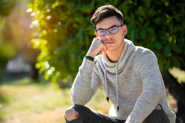 Giovane con maglione grigio seduto nel parco