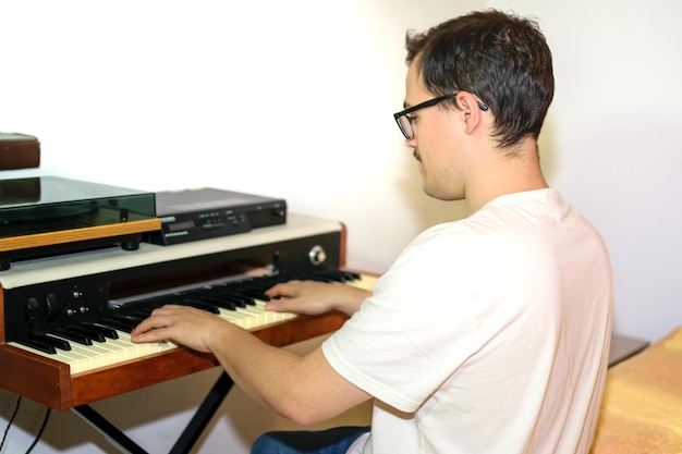 Giovane con occhiali e maglietta bianca che compone e suona il pianoforte nella sua camera da letto