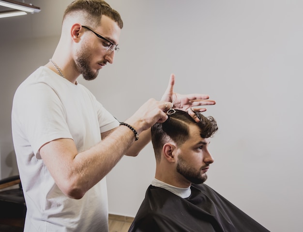 Giovane con taglio di capelli alla moda al negozio di barbiere. Il barbiere fa la pettinatura e la barba.