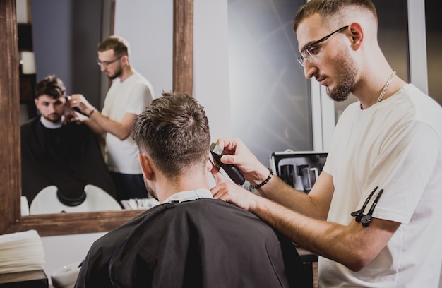 Giovane con taglio di capelli alla moda al negozio di barbiere. Il barbiere fa taglio di capelli e barba.