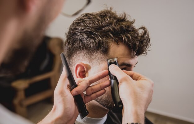 Giovane con taglio di capelli alla moda al negozio di barbiere. Il barbiere fa taglio di capelli e barba.