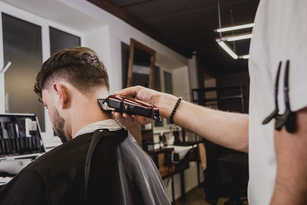 Giovane con taglio di capelli alla moda al negozio di barbiere. Il barbiere fa taglio di capelli e barba.