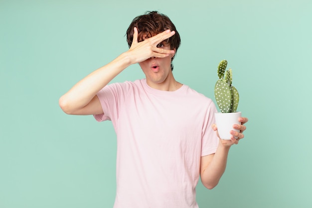 Giovane con un cactus che sembra scioccato, spaventato o terrorizzato, coprendo il viso con la mano