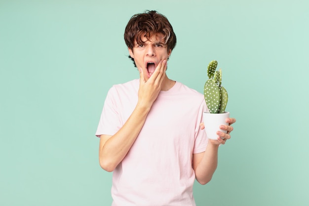 Giovane con un cactus con la bocca e gli occhi spalancati e la mano sul mento