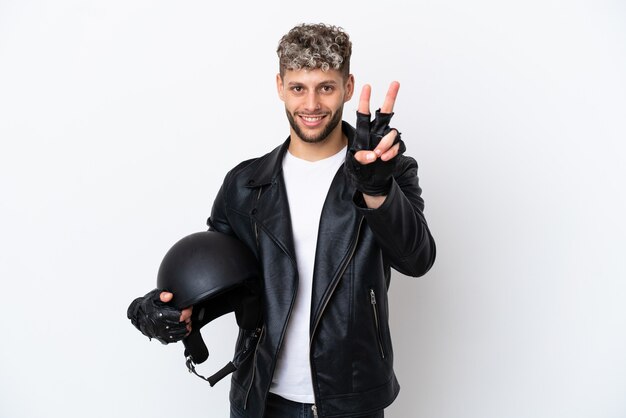 Giovane con un casco da motociclista isolato su sfondo bianco che sorride e mostra il segno della vittoria