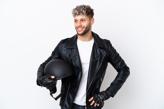 Giovane con un casco da motociclista isolato su sfondo bianco in posa con le braccia all'anca e sorridente