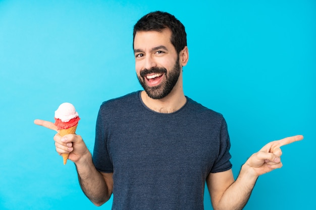 Giovane con un gelato della cornetta sopra la parete blu isolata che indica barretta ai laterali e felice