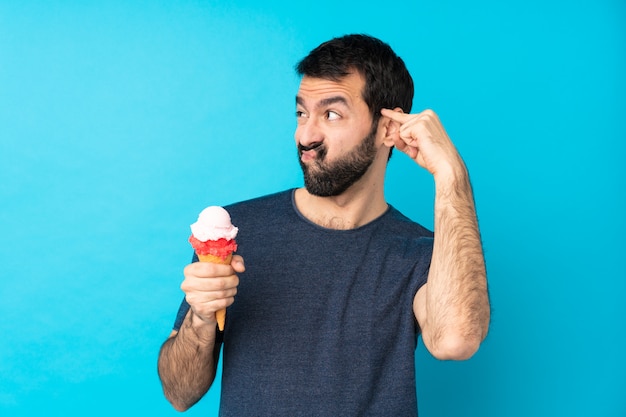 Giovane con un gelato di cornetta sul blu che fa il gesto della follia mettendo il dito sulla testa