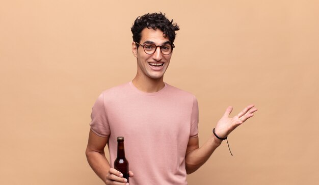 Giovane con una birra che si sente felice, sorpreso e allegro, sorridente con atteggiamento positivo, realizzando una soluzione o un'idea