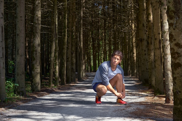 Giovane con una figura atletica in pantaloncini, legare i lacci delle scarpe prima di attraversare la foresta