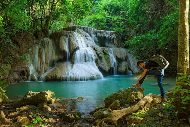 Giovane con zaino in piedi vicino a una cascata nella foresta Escursionista maschio nella natura durante la pioggia