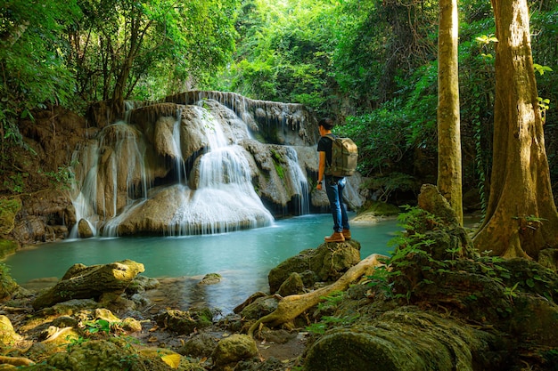 Giovane con zaino in piedi vicino a una cascata nella foresta Escursionista maschio nella natura durante