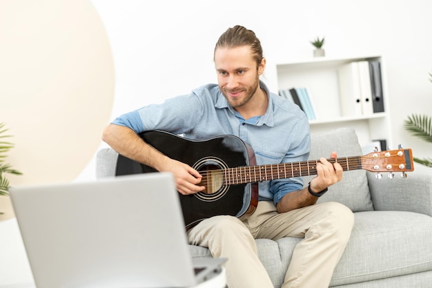 Giovane concentrato a casa con il portatile che suona la chitarra
