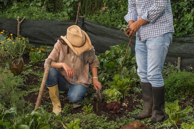 Giovane contadina accovacciata accanto a un uomo con gli stivali in un orto