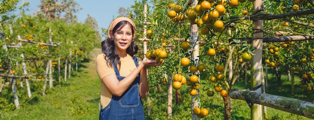 Giovane contadina asiatica in piedi che tiene frutta arancione con sorridente in giardino