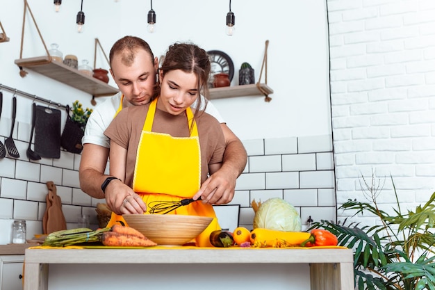 Giovane coppia adorabile che cucina un piatto in cucina e si abbraccia