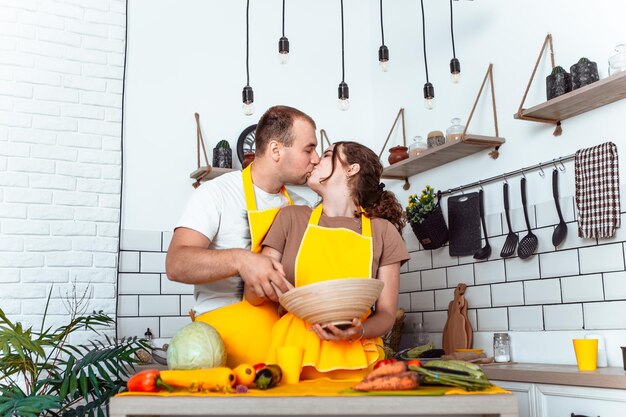 Giovane coppia adorabile che cucina un piatto in cucina e si bacia e si abbraccia