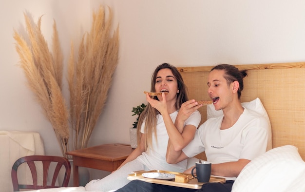 Giovane coppia al mattino facendo colazione romantica a letto nel giorno di San Valentino come relazioni felici