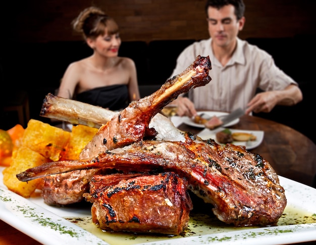 Giovane coppia al ristorante che mangia bistecca, carré di agnello.