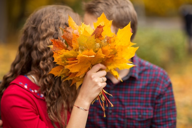 Giovane coppia baci dietro un bouquet di foglie d'autunno.