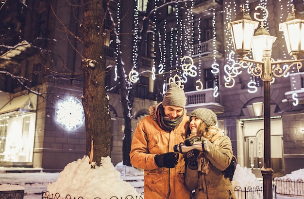 Giovane coppia che beve tè caldo nel centro della città sotto l'illuminazione invernale