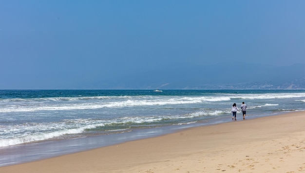 Giovane coppia che cammina sulla spiaggia di sabbia Onde del mare dell'oceano blu chiaro cielo blu in una soleggiata giornata primaverile