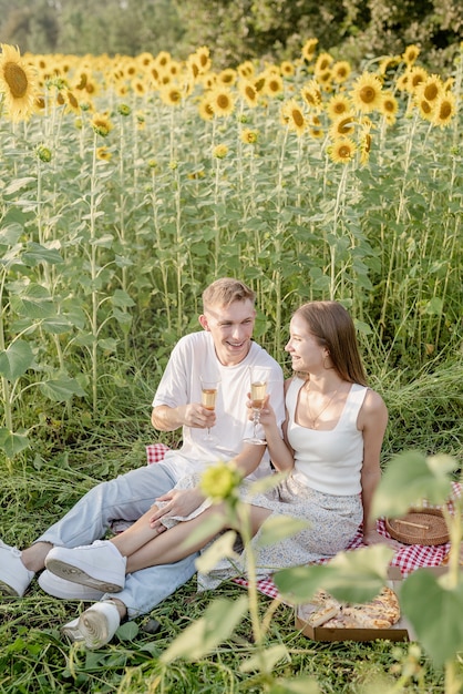 Giovane coppia che fa un picnic sul campo di girasoli al tramonto