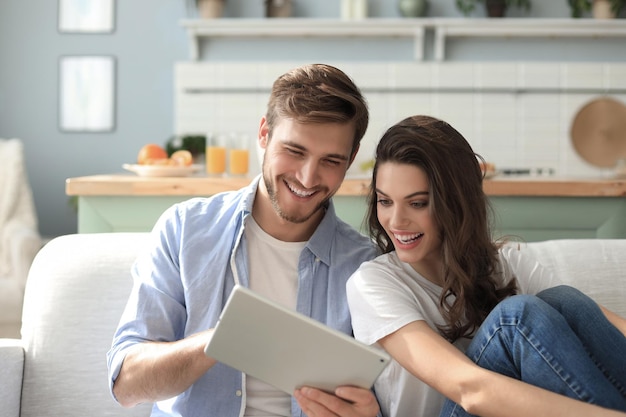 Giovane coppia che guarda contenuti multimediali online in un tablet seduto su un divano nel soggiorno.