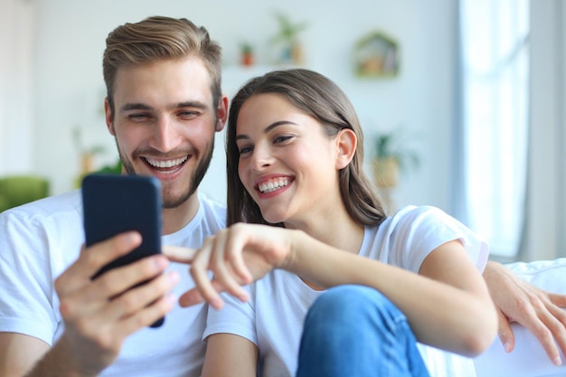 Giovane coppia che guarda contenuti online in uno smartphone seduto su un divano a casa in soggiorno.