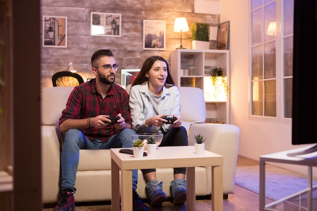 Giovane coppia che si diverte mentre gioca ai videogiochi in televisione. Coppia seduta sul divano.