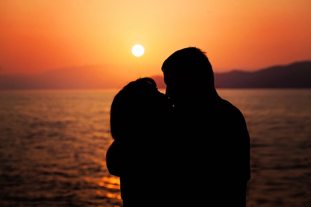 Giovane coppia che si gode il tramonto sulla spiaggia bacia la siluetta dell'uomo e della donna