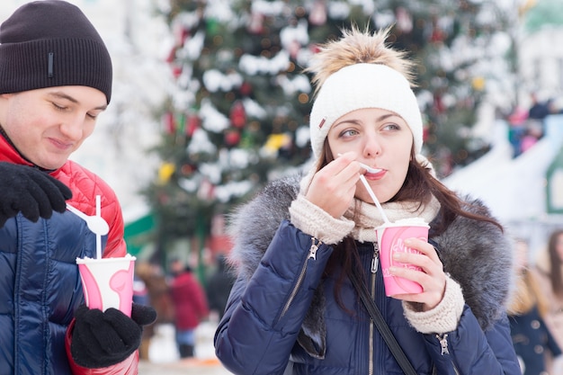 Giovane coppia che si gode un cappuccino caldo in inverno mentre si trova all'aperto durante un festival di Natale o un mercato sorseggiando da tazze da asporto