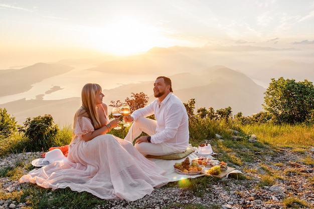 Giovane coppia con un picnic al tramonto in montagna, felice, ridendo